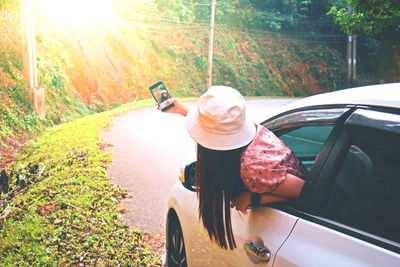 Woman taking selfie with mobile phone while leaning out from car window