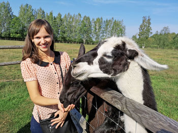 Portrait of smiling woman feeding alpacas at farm 