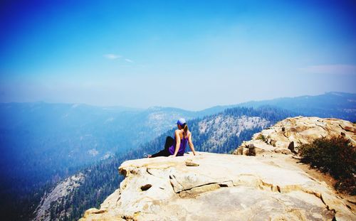 Rear view of woman looking at view while sitting on mountain