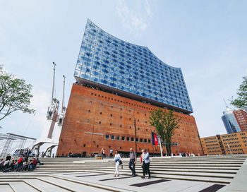 People walking on road by buildings against sky in city
