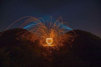 Firework display on field against sky at night