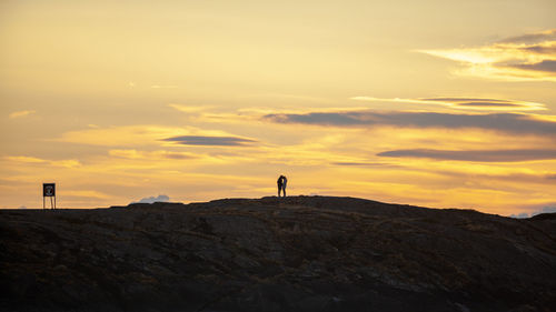 Couple kissing rock against sky during sunset