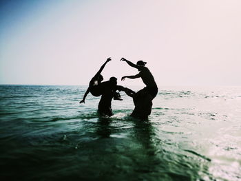 SILHOUETTE MEN STANDING AT SEA SHORE AGAINST CLEAR SKY