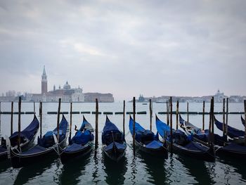 Gondolas moored at canal against sky