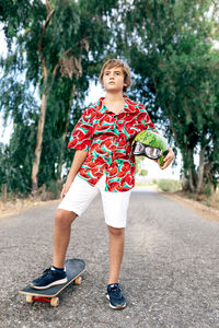 Focused boy in stylish apparel on skateboard with decorative watermelon helmet and protective eyeglasses looking away on roadway