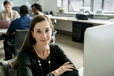 Portrait of businesswoman sitting desk while colleagues discussing in background