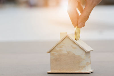 Cropped hand putting gold coin in house shaped piggy bank on table