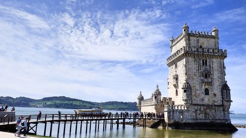 People at historic belem tower in sea against sky