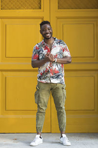 Happy young man with hands clasped standing against closed yellow doors