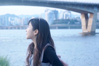 Woman looking away against river in city