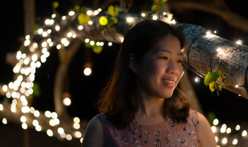 Portrait of smiling woman with illuminated lights at night