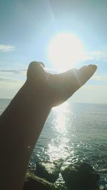 Person hand by sea against bright sun