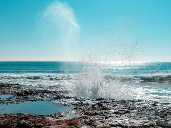 Scenic view of sea splashing on rocks against clear sky 