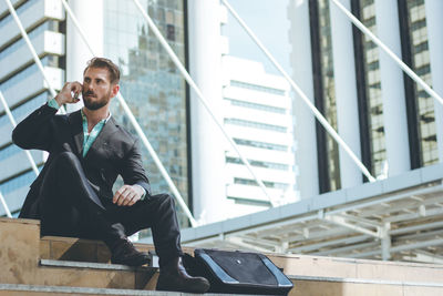 Full length of businessman talking on phone by modern buildings