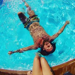 Low section of woman at poolside with man swimming in pool