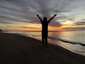 Rear view of woman walking at beach against sky during sunset