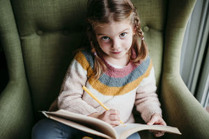 Cute girl doing homework while sitting on chair at home