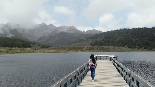 Rear view of woman walking on pier over lake against sky