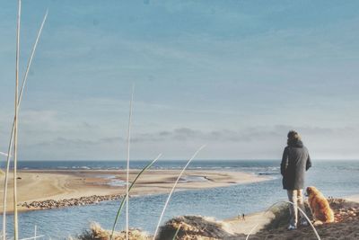 Woman standing with dog looking at beach against sky