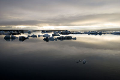 Scenic view of frozen glacial lake with lotteria iceberg against sky during sunset