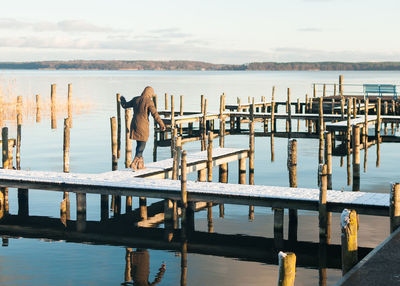 Rear view of woman walking on snow covered jetty in lake against sky