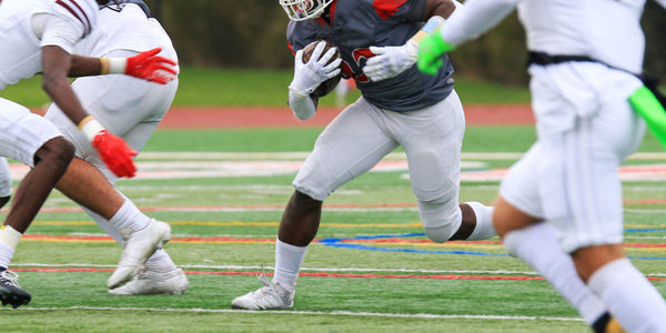 Front view of a high school football running back running into the whole in the defense.