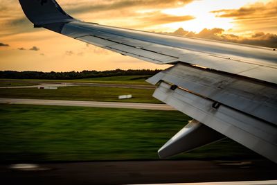 Close-up of airplane wing against sky during sunset