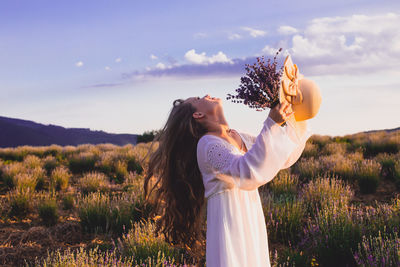 Woman standing by flowers on field against sky