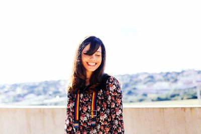 Smiling young woman standing at rooftop against clear sky