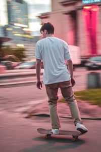 Rear view of man skateboarding on road in city