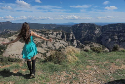 Rear view of woman standing on rock against sky