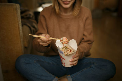 Midsection of woman eating food while sitting on floor at home