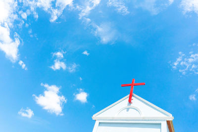Red cross over the church with beautiful day, blue sky and clouds