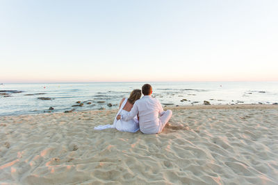 Rear view of men sitting on beach against clear sky