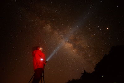 Low angle view of person with flashlight against star field at night