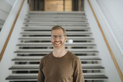 Portrait of happy mature professor standing against steps in university