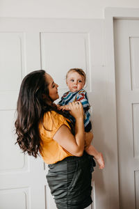Mother carrying son while standing by door at home