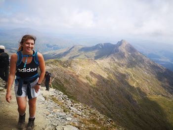 Full length portrait of smiling man standing on mountain against sky