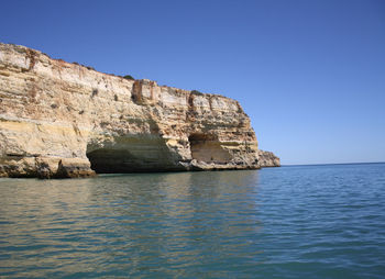 Rock formation in sea against clear blue sky