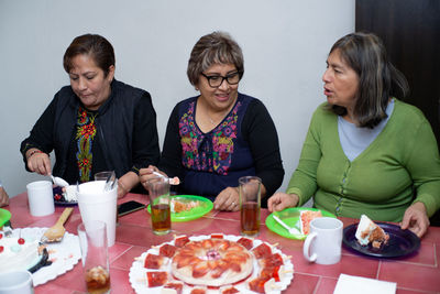 An older man with his friends celebrating his birthday, eating cake at an indoor party. old birthday