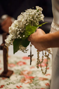 Midsection of bridegroom holding bouquet and rosary beads during wedding