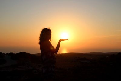 Silhouette woman standing by tree against sky during sunset