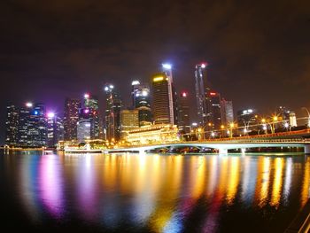 Illuminated buildings by river against sky at night
