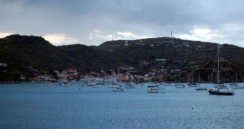 Sailboats moored on sea by city against sky