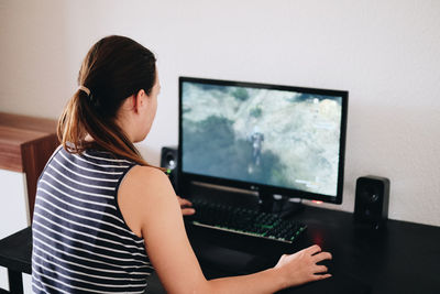 Rear view of woman using computer on table at home