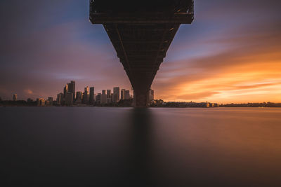 Illuminated city by sea against sky at sunset