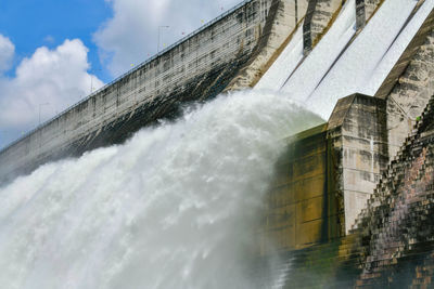 Water splashing on dam against sky