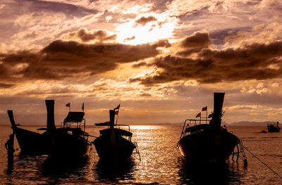 Silhouette boats moored in sea against sky during sunset