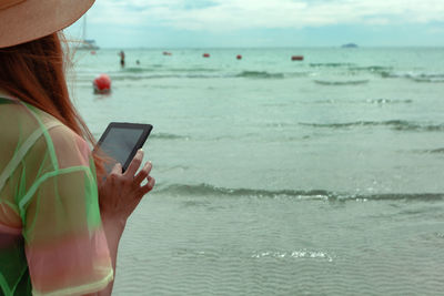 Midsection of woman using digital tablet while standing at beach