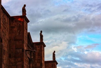 Low angle view of statue by building against sky